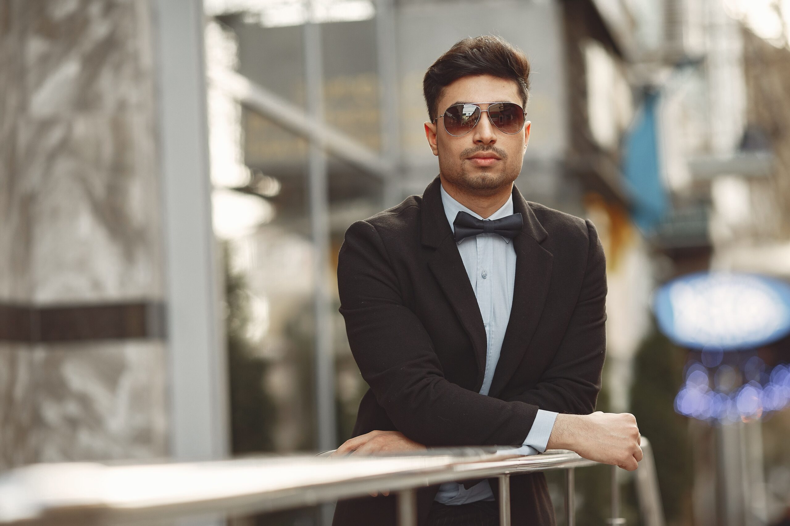 A stylish man in sunglasses and bow tie, exuding confidence in an urban setting.